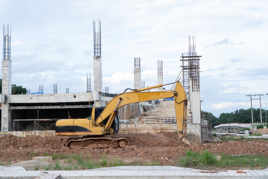 Yellow heavy machinery excavator operates at construction site near concrete building structure, conveying ambitious determination and hopeful progress during real estate development