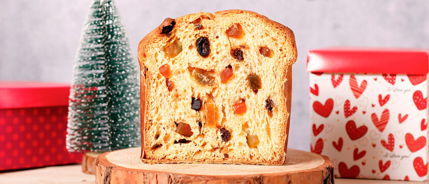 Traditional sliced Christmas panettone with candied fruit and raisins on festive wooden base.