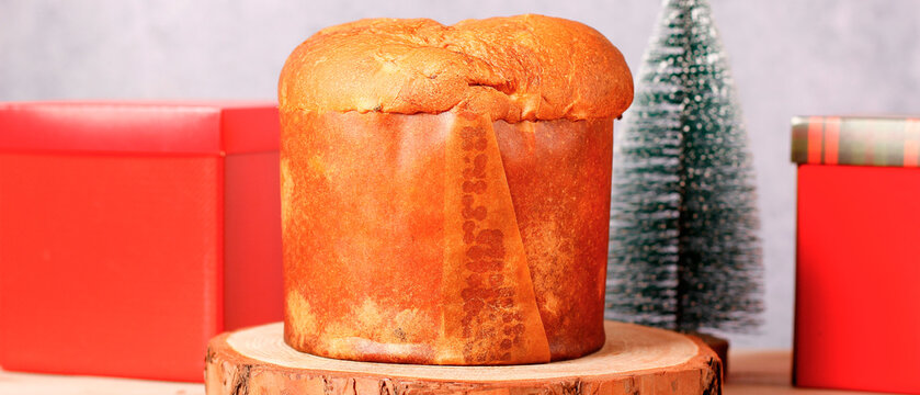 Classic Christmas panettone on a wooden stand on a table, with gifts and a Christmas tree in the background.