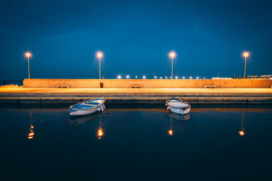 Two small boats moored in a harbour at night under street lamps, Puglia, Italy