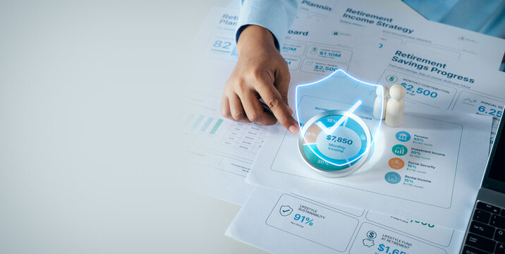 Financial planner pointing at retirement income strategy document with digital shield and checkmark icon on white desk, concept of retirement savings progress and financial security.