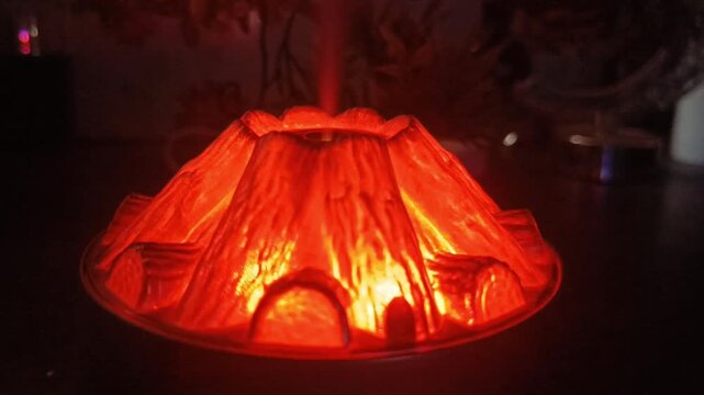 Volcano shaped aroma diffuser glowing red with rising mist on dark table