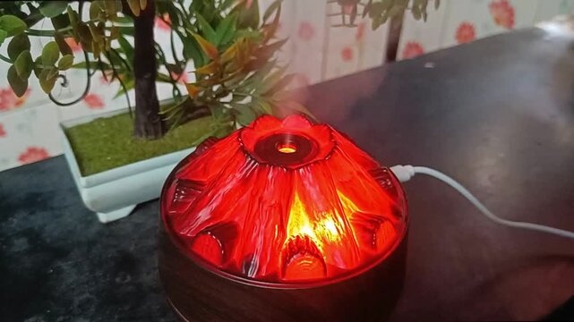 Volcano mist diffuser glowing red beside faux bonsai plant with USB cord visible
