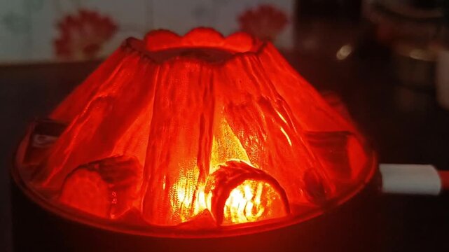 Glowing red volcano shaped diffuser emitting mist on dark wooden desk