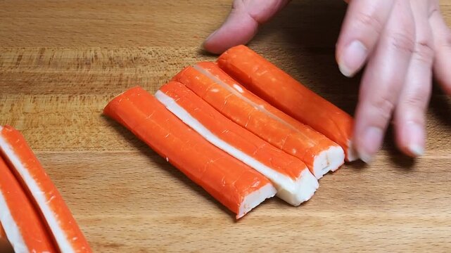 The cook cuts crab sticks on a cutting board into slices. closeup.