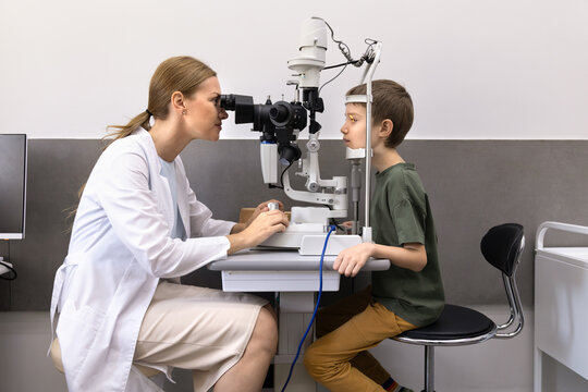 Female ophthalmologist using slit lamp biomicroscope for examination of eyes boy patient in optical clinic. Eyecare diagnostics procedure, professional eyesight checkup of child, vision assessment