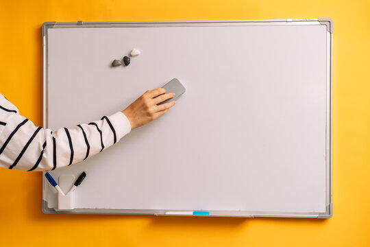 Hand wiping the middle of a blank whiteboard with a gray eraser.