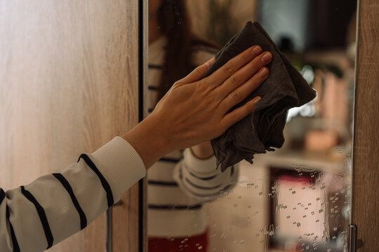 Hand wiping the upper mirror with a gray cloth in close view.