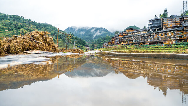Miao village and misty mountains reflected in calm water near Xijiang, Guizhou, China