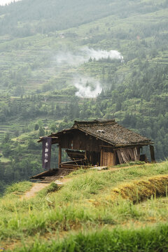 Old wooden house on a green hillside with mist rising behind, near Xijiang, Guizhou, China