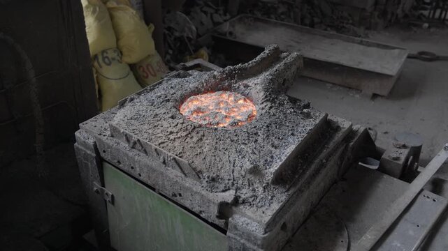 A circular furnace opening reveals an orange metal bath partly covered by a dark surface layer within a rough grey refractory surround.