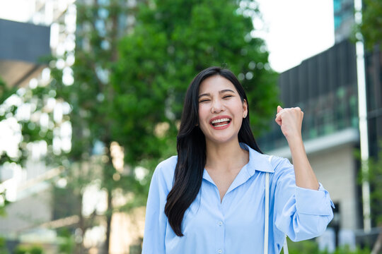 Portrait of Asian excited businesswoman looking at camera outdoors in city. 
