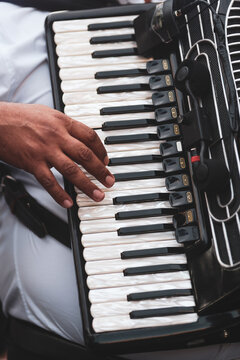 A musician's hand rests on the pearl-white keys of a black piano accordion, with clip-on microphones capturing every note of a live performance