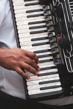 A musician's hand rests on the pearl-white keys of a black piano accordion, with clip-on microphones capturing every note of a live performance