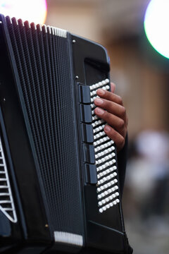 A musician's hand rests on the pearl-white keys of a black piano accordion, with clip-on microphones capturing every note of a live performance