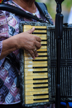 A musician's hand rests on the pearl-white keys of a black piano accordion, with clip-on microphones capturing every note of a live performance