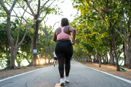 Rear view of Black plus-size woman jogging along pathway in garden. 