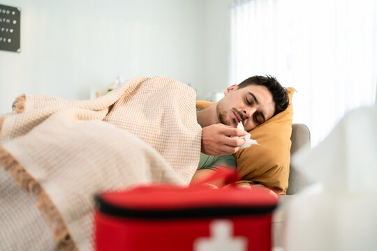 Latino sick man feeling cold while lying on sofa in living room at home.