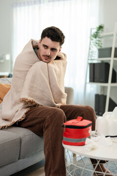 Latino sick man feeling cold while sitting on sofa in living room at home.