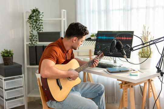 Young Latino man play guitar and produce electronic soundtrack at home. 