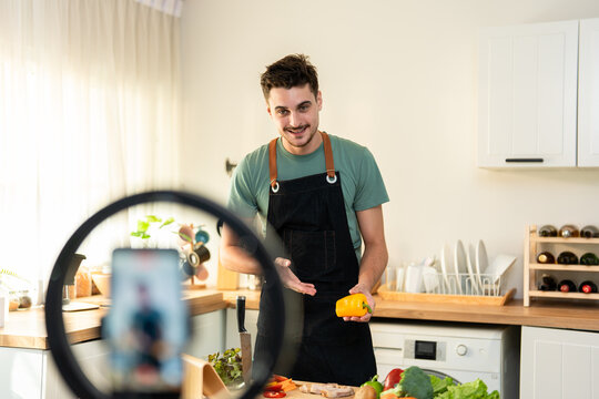 Latino man live streaming with mobile phone while cooking food in kitchen. 