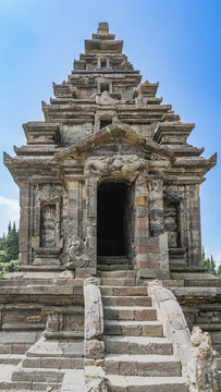 Ancient Hindu architecture. Arjuna temple complex. A stone sanctuary with a stepped roof, carvings, and bas‑reliefs of Kala Makara. Staircase to the entrance. Blue sky. Indonesia. Java. Dieng Plateau.