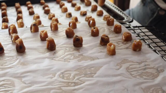 Close up baker hands piping small sweet dough onto baking paper sheet tray. Pastry chef piping cookies or candy drops, homemade bakery confectionery food preparation production concept.