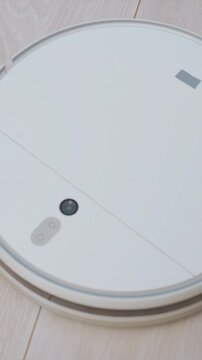 Round automated home cleaning device moving smoothly over wooden flooring. robotic cleaner features illuminated control icons emphasizing its modern design and functionality in domestic