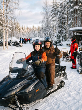 Happy father and son riding snowmobile on winter safari in snowy forest