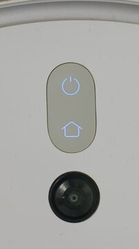 Close up view focusing on illuminated power and home icons centered within oval button below which is circular lens. device remains stationary with consistent lighting