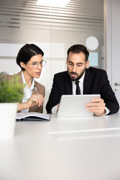 Focused diverse colleagues reviewing business project or information on digital tablet, planning strategy, working on task. Professional mentorship, client and manager discussion in corporate office