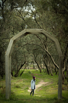 A woman walks beneath a wooden arch and along a winding path through a tranquil woodland, Donald, Victoria, Australia