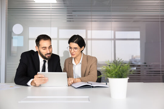 Multiethnic colleagues reviewing information on digital tablet, making business data analysis, developing marketing strategy, planning, collaborating on online project, working in office meeting room