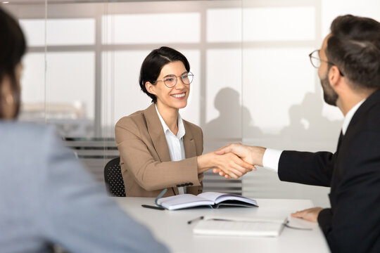 Smiling businesswoman shake hands with business partner at office desk, concluding professional briefing, confirming agreement, finalizing formal discussion, recruitment interview, consulting meeting