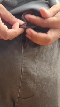 Close up hands tying drawstring knot on waistband of casual pants. Person adjusting and fastening waist cord string on trousers, getting dressed and lifestyle clothing routine concept