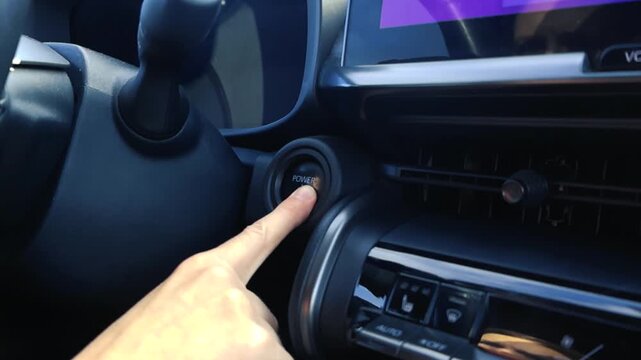 Close up view of a driver's finger pushing the power button to start the engine of a modern electric car, activating the futuristic digital dashboard and infotainment system inside the cockpit
