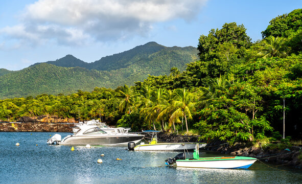 Boats anchored along the lush green tropical coastline near Port de Trois-Rivieres with green volcanic mountains in Basse-Terre, Guadeloupe.