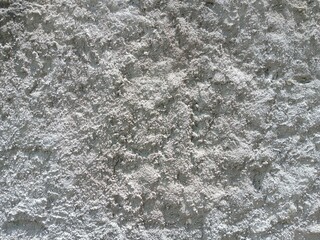Texture of a light grey roughcast stucco wall with a heavily textured, uneven plaster surface illuminated by bright sunlight © Ricko Destu