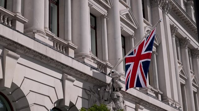 Union Jack flag ripples on the fa&ccedil;ade of Sofitel London St James, framed by ornate white stone columns in soft daylight.