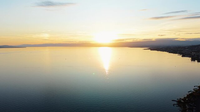 Drone pulls back revealing a wide sunset view over Lake Geneva near Cully