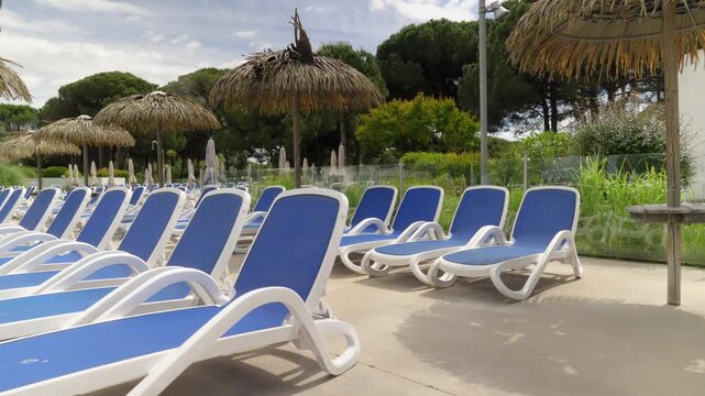 Empty blue sun loungers by a glass pool fence at a holiday club outdoor area