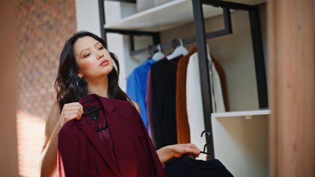 Woman choosing outfit wardrobe closet. Asian shopper comparing blazers hangers.