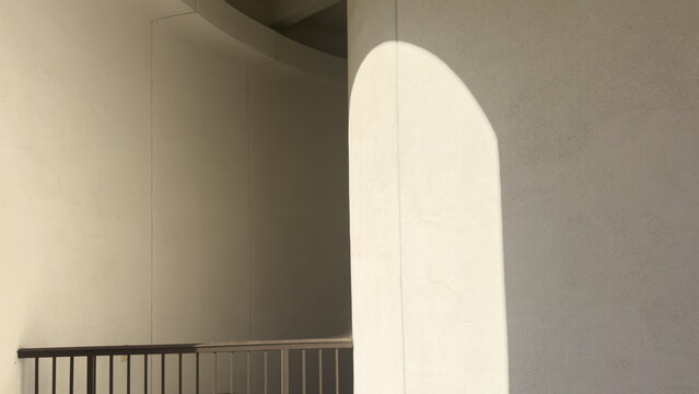 sunlight casts an arched highlight across a smooth beige stucco column beside a dark metal railing