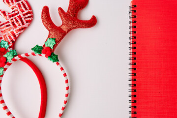Red reindeer headband with antlers alongside a spiral notebook on a white background, useful for holiday planning, shopping lists, and festive notes.  © Ryan