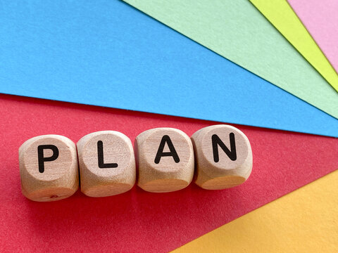 Wooden blocks spelling PLAN on colorful geometric paper background.