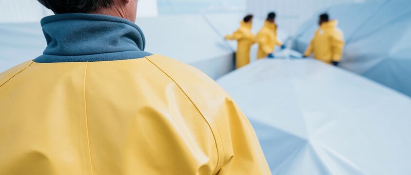 Yellow oilskin jacket on a boatyard worker, weathered waterproof gear in a coastal storm setting with copy space for mockup branding