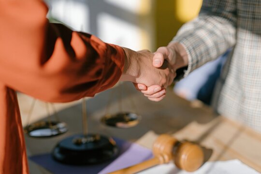 European lawyer hands shaking in a warm agreement, featuring a wooden gavel and scales on a sunny desk for business and legal services