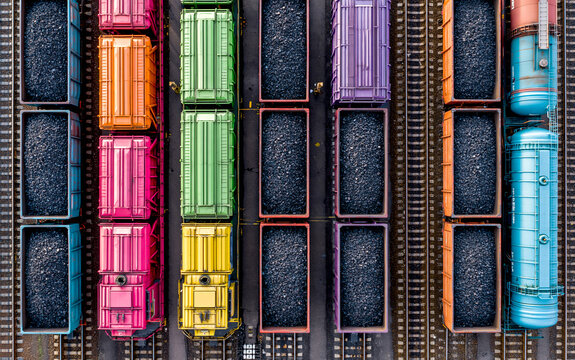 Colorful freight train cars filled with coal parallel railway tracks, industrial transportation scene with vibrant wagon, overhead view, energy supply and resource, organized railway yard