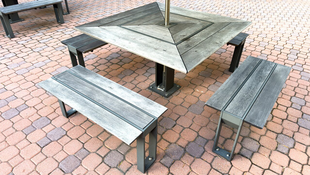 a grey slatted wood picnic table and matching benches sit on interlocking reddish pavers in an outdoor courtyard patio
