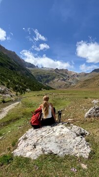 woman hiker sitting on rock with backpack in mountain valley landscape under blue sky